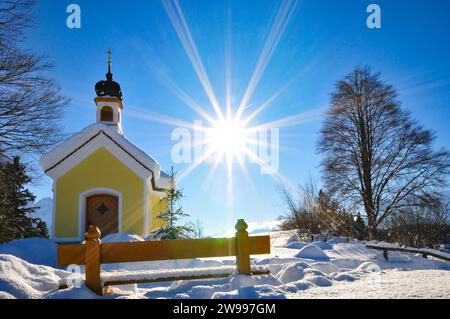 Ripresa in controluce della Cappella Maria ricoperta di neve sul Buckelwiesen Werdenfelser Land vicino a Garmisch in un idillio del vento, Baviera, Germania, Europa Foto Stock