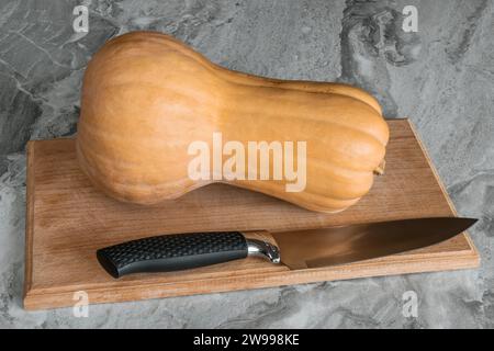 Zucca Butternut (Cucurbita moschata), nota come zucca butternut o gramma adagiata su un tagliere con un coltello Foto Stock