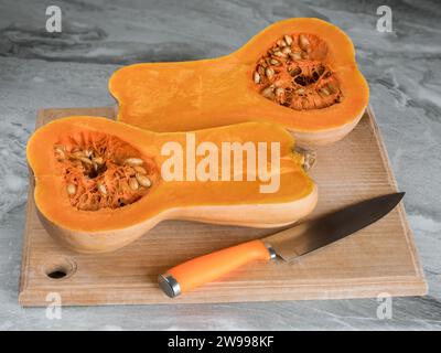 Zucca Butternut (Cucurbita moschata), nota come zucca butternut o gramma tagliato a metà disteso su un tagliere Foto Stock