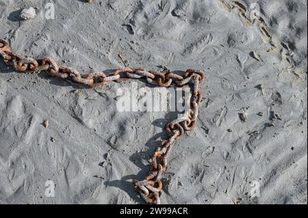 Dettaglio di una vecchia catena arrugginita sul terreno argilloso del fondo marino durante la bassa marea Foto Stock