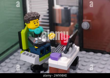 Tambov, Federazione Russa - 25 dicembre 2023 Una minifigura di un giocatore di videogiochi Lego con un gamepad seduto su una sedia da gioco e con cui gioca ai videogiochi Foto Stock