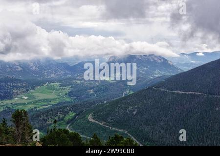 Un pittoresco paesaggio di dolci colline ricoperte di prati lussureggianti e alberi, con maestose montagne in lontananza Foto Stock