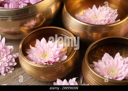 Ciotole tibetane con acqua e bellissimi fiori su un tavolo di legno, primo piano Foto Stock