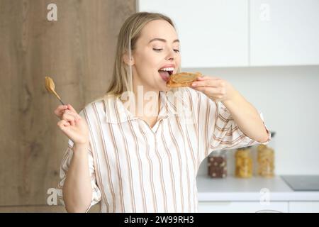 Giovane donna che mangia toast con burro di noci in cucina Foto Stock