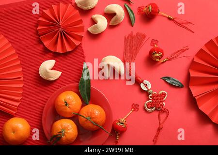 Composizione con tifosi di carta, mandarini, biscotti della fortuna e simboli cinesi su sfondo rosso. Festeggiamenti per il nuovo anno Foto Stock