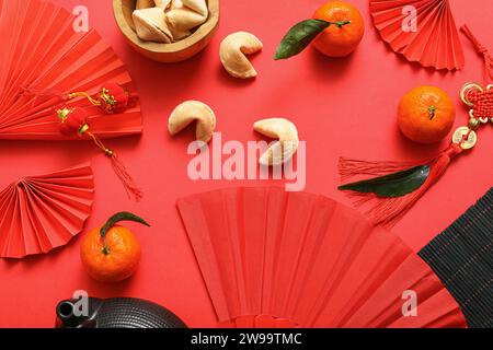 Composizione con tifosi di carta, biscotti della fortuna, mandarini e simboli cinesi su sfondo rosso. Festeggiamenti per il nuovo anno Foto Stock