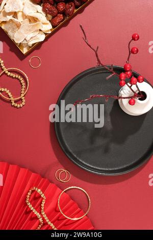 Il set di gioielli è esposto su uno sfondo rosso con marmellata di zenzero, giuggiola, ventola di carta rossa, vaso di fiori e un piatto nero. Spazio di copia per gli annunci e visualizzazione Foto Stock