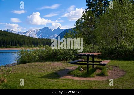 Un tavolo da picnic sul bordo di un lago che si affaccia sulle montagne canadesi in Alberta Foto Stock
