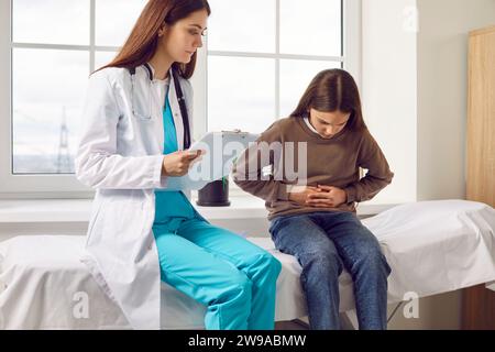 Bambina seduta nello studio del medico che punta al suo stomaco durante l'esame medico in clinica. Foto Stock