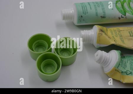 Cosmetici da donna, tre tubi di plastica usati di crema viso con tre cappucci verde chiaro disposti su uno sfondo di plastica bianca. Foto Stock