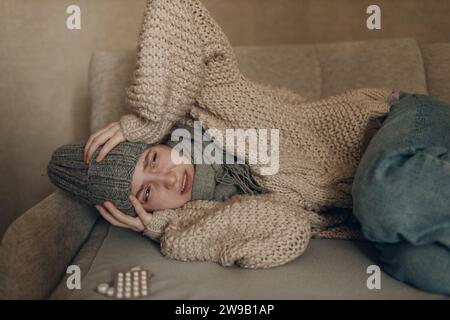 Giovane donna che indossa sciarpa ha malattia malata di influenza freddo a casa indoor sul divano Foto Stock