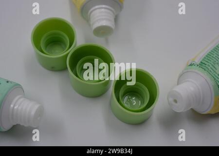 Cosmetici da donna, tre tubi di plastica usati di crema viso con tre cappucci verde chiaro disposti su uno sfondo di plastica bianca. Foto Stock