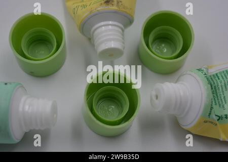 Cosmetici da donna, tre tubi di plastica usati di crema viso con tre cappucci verde chiaro disposti su uno sfondo di plastica bianca. Foto Stock