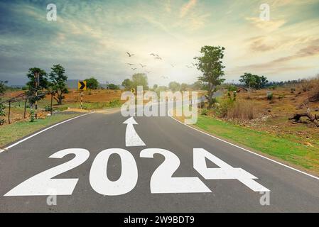 Concetto di Capodanno 2024. Testo 2024 scritto sulla strada in mezzo alla strada al tramonto. Inizio anno nuovo Foto Stock