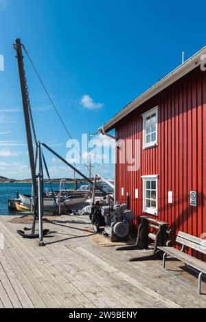 Magazzini con tipiche facciate in legno rosso e barche da pesca nel porto di Skärhamn nell'arcipelago dell'isola di Tjörn in estate, Svezia Foto Stock