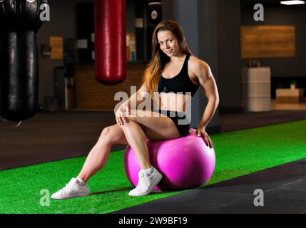 Il campione di bodybuilding si allena in palestra con un'enorme palla rosa. Supporti misti Foto Stock