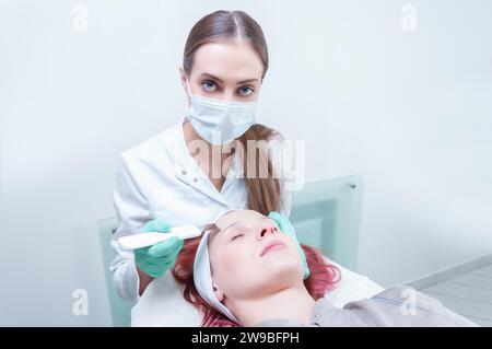 L'estetista lava il viso del paziente prima di pelarlo. Concetto di cura della pelle. Supporti misti Foto Stock