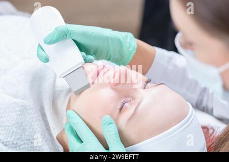 L'estetista pulisce il viso del paziente con un dispositivo a ultrasuoni. Salone di bellezza. Supporti misti Foto Stock