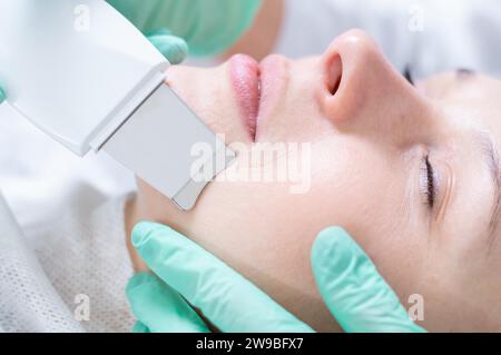 Giovane bella donna che riceve trattamenti nei saloni di bellezza. Procedura di pulizia a ultrasuoni. Cosmetologia hardware. Supporti misti Foto Stock