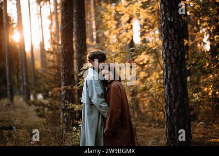 Bella coppia alla moda innamorata nella foresta al tramonto in autunno, appuntamento romantico in impermeabili, uomo e donna alla moda Foto Stock