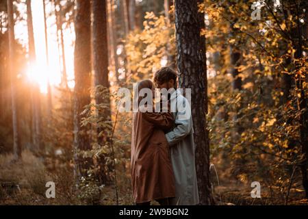 Bella coppia alla moda innamorata nella foresta al tramonto in autunno, appuntamento romantico in impermeabili, uomo e donna alla moda Foto Stock