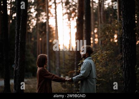 Bella coppia alla moda innamorata nella foresta al tramonto in autunno, appuntamento romantico in impermeabili, uomo e donna alla moda Foto Stock