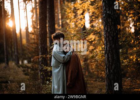 Bella coppia alla moda innamorata nella foresta al tramonto in autunno, appuntamento romantico in impermeabili, uomo e donna alla moda Foto Stock