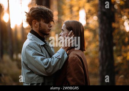 Bella coppia alla moda innamorata nella foresta al tramonto in autunno, appuntamento romantico in impermeabili, uomo e donna alla moda Foto Stock