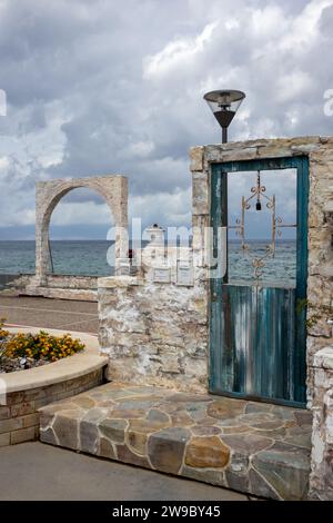 Mostra di dettagli tradizionali, utilizzati nell'architettura greca. Cancello con colonne e arco, accanto al mare. Porta con porta in legno nella parte anteriore Foto Stock
