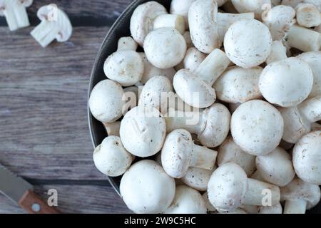 Funghi champignon bianchi (agaricus bisporus) in una ciotola con coltello su un tavolo di legno. Vista dall'alto, primo piano. Foto Stock