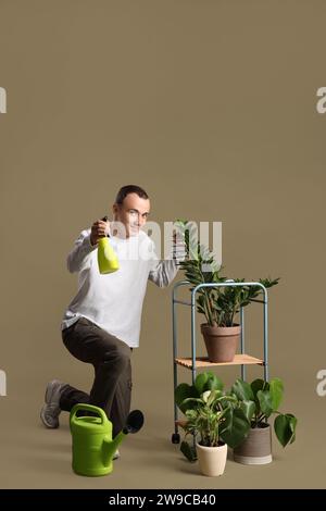 Giovane che spruzza acqua sulle piante su fondo verde Foto Stock