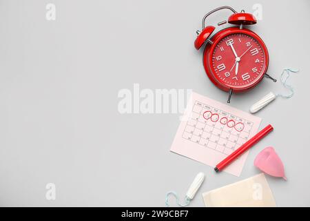 Composizione con calendario mestruale, prodotti per l'igiene femminile e sveglia su sfondo grigio Foto Stock