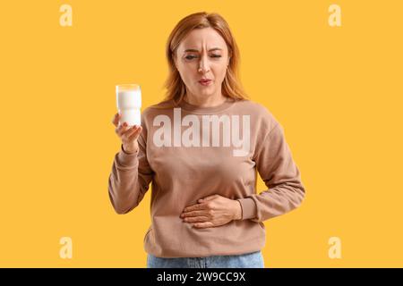 Donna matura con un bicchiere di latte che soffre di mal di stomaco su sfondo giallo Foto Stock