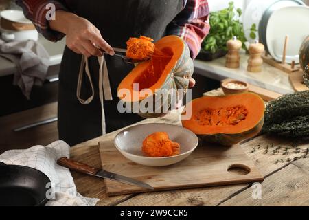 Donna che rimuove i semi dalla zucca cruda al tavolo di legno in cucina, primo piano Foto Stock