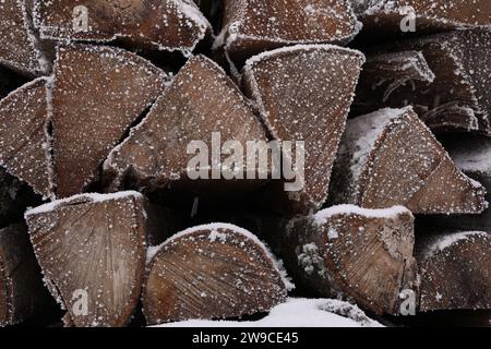 Legna da ardere impilata con neve e brace come sfondo, primo piano Foto Stock