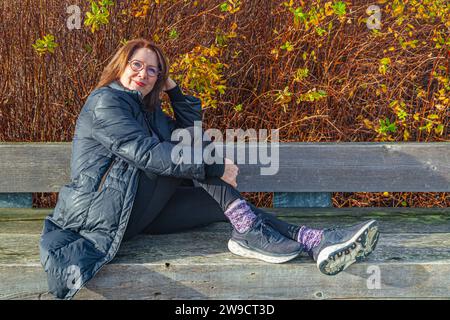 Attraente nonna che si rilassa su una panchina di legno a Richmond, British Columbia, Canada Foto Stock