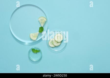 Vista dall'alto delle fette di cetriolo fresco decorate su piatti di petri e del podio trasparente su sfondo blu pastello. Scena minima per la pubblicità. Centro benessere vuoto Foto Stock