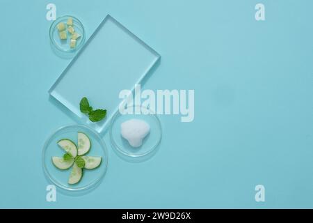 Vista dall'alto dei piatti di podio e petri trasparenti contenenti fette di cetriolo decorate su sfondo blu con spazio per la copia. Piedistallo per prodotti cosmetici Foto Stock