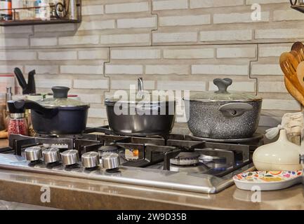 Cucina vivace con pentole e coperchi diversi su una stufa a gas, fiamme che bruciano, mentre il cibo delizioso viene preparato a casa, creando un ambiente accogliente e accogliente Foto Stock