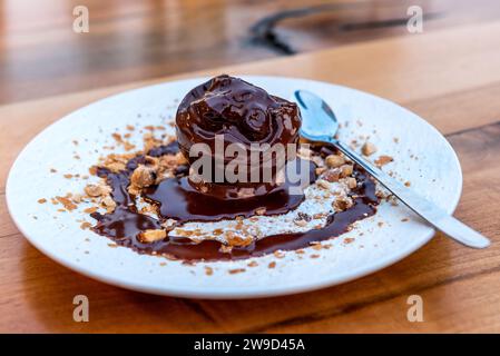 Delizioso cucchiaio per gelato da vicino sul piatto con condimento al cioccolato fuso e nocciole su un tavolo rustico in legno Foto Stock
