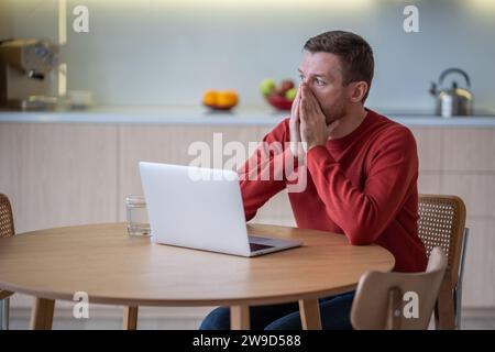 Un uomo stressato e preoccupato siede con un notebook che si sente burnout, apatia, problemi di concentrazione a casa. Foto Stock