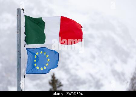 Le bandiere dell'Italia e dell'UE (Unione europea) volano insieme sullo sfondo delle montagne innevate italiane. Dolomiti d'inverno. Foto Stock