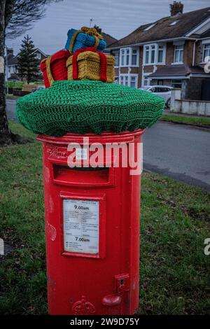 Scatole regalo di Natale in maglia decorativa sulla parte superiore di una tradizionale cassetta per lettere rossa del Regno Unito in una strada periferica del Galles. Dicembre 2023. Foto Stock