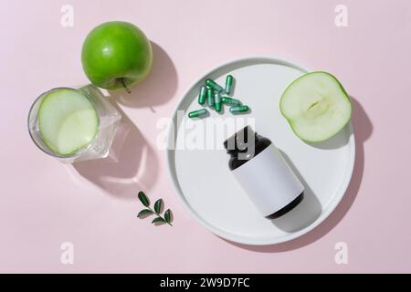 Scena minimalista per la pubblicità e il branding dei prodotti. Una bottiglia di medicina, pillole e mele verdi decorate su sfondo rosa. Vista dall'alto, spazio per des Foto Stock