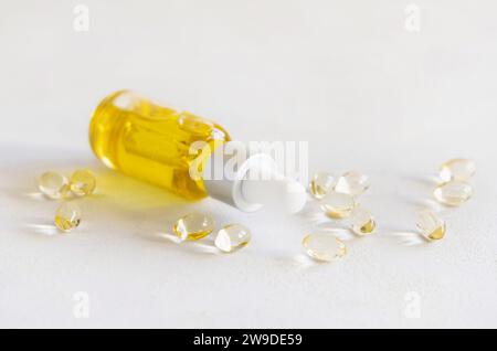 Olio giallo in una bottiglia contagocce e capsule su un tavolo bianco da vicino. Integratore alimentare. Composizione minima Foto Stock