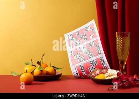 Piatti in legno contenenti mandarini e caramelle secche. Una scheda bingo con un bicchiere. Il Capodanno lunare è la festa più importante di voi Foto Stock