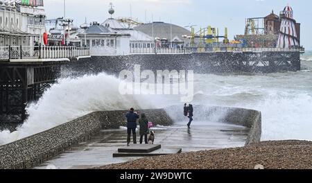 Brighton Regno Unito 27 dicembre 2023 - i visitatori si bagnano mentre le onde si infrangono sul lungomare di Brighton vicino al molo mentre Storm Gerrit batte la Gran Bretagna oggi con avvisi meteo emessi in tutto il paese : Credit Simon Dack / Alamy Live News Foto Stock