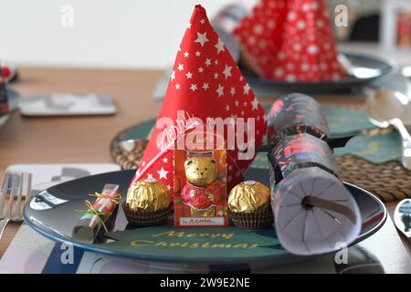 Un tavolo per le feste, cracker natalizi, tovaglioli di buon Natale, Ferrero Rocher e orsacchiotto al cioccolato Lindt. Foto Stock