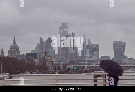 Londra, Regno Unito. 27 dicembre 2023. Una passeggiata pedonale attraverso il Waterloo Bridge passando davanti allo skyline della City di Londra, il quartiere finanziario della capitale, tra forti venti e pioggia mentre Storm Gerrit colpisce il Regno Unito. Credito: Vuk Valcic/Alamy Live News Foto Stock