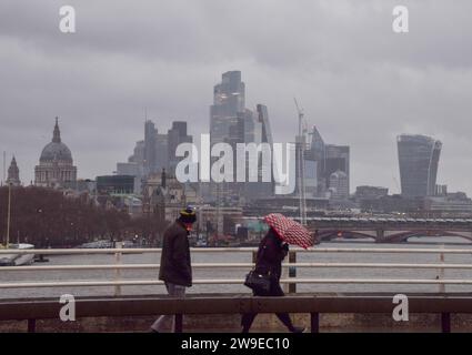 Londra, Regno Unito. 27 dicembre 2023. La gente cammina attraverso il Waterloo Bridge passando davanti allo skyline della città di Londra, il quartiere finanziario della capitale, tra venti forti e pioggia, mentre Storm Gerrit colpisce il Regno Unito. Credito: Vuk Valcic/Alamy Live News Foto Stock